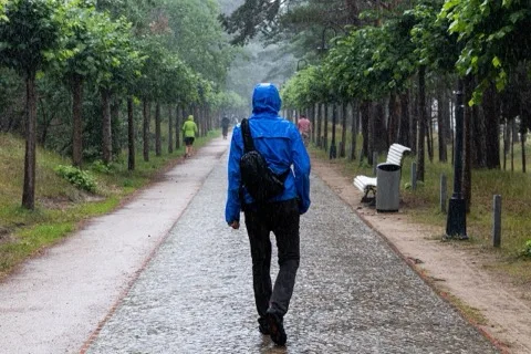 Person mit blauer Regenjacke mit Kapuze unterwegs im Regen