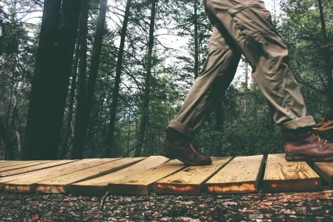 Trekkinghose und Wanderschuhe beim Gehen über einen Holzsteg im Wald